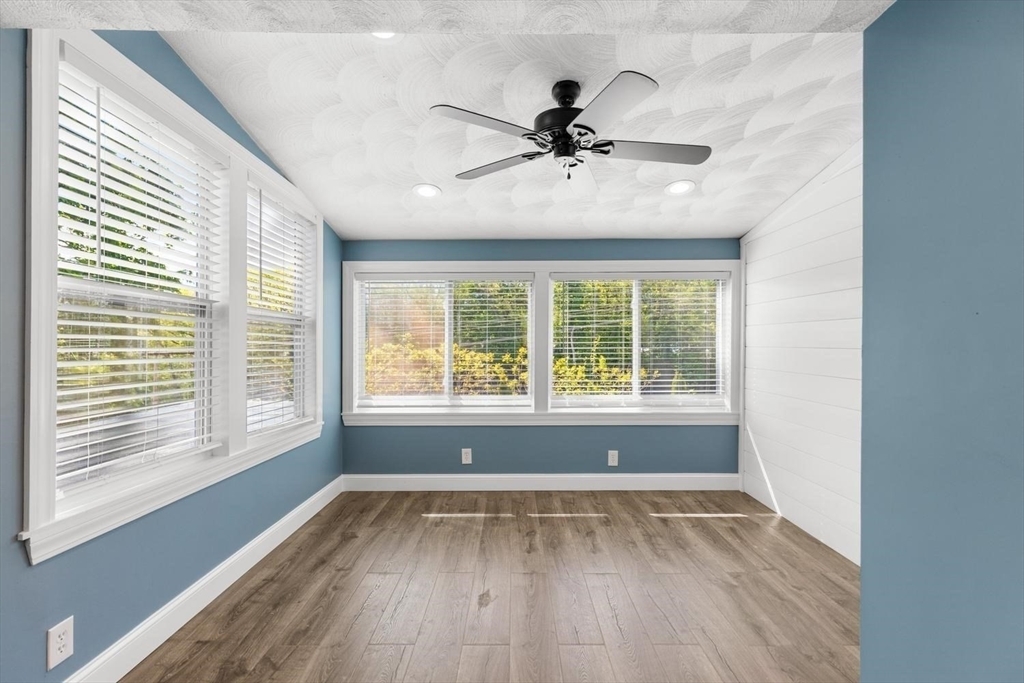 A bright blue-walled bonus room at 53 Longhill Rd wrapped with windows on two walls, a black ceiling fan, and wood-look floors letting in daylight